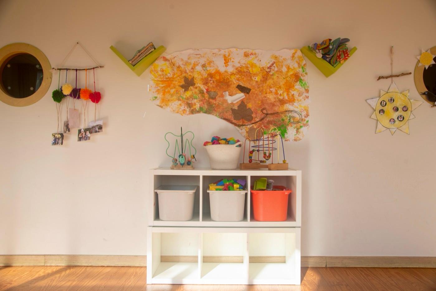 Rincón de juego con las cajas de juguetes y el mural de otoño en la pared