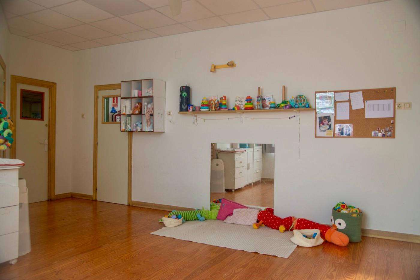 Aula de 2 a 3 años con la ventana de espejo, la estantería de juguetes y el corcho
